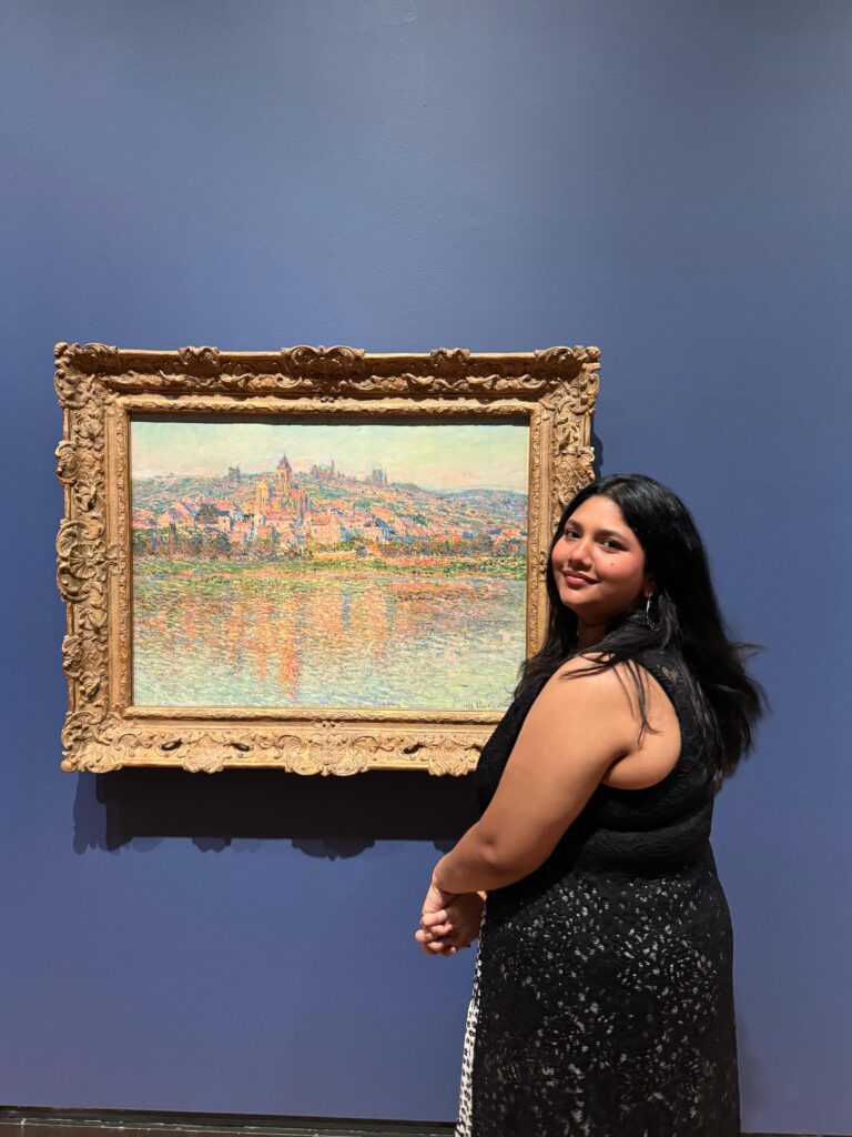 Amatullah standing next to a painting in an art gallery.