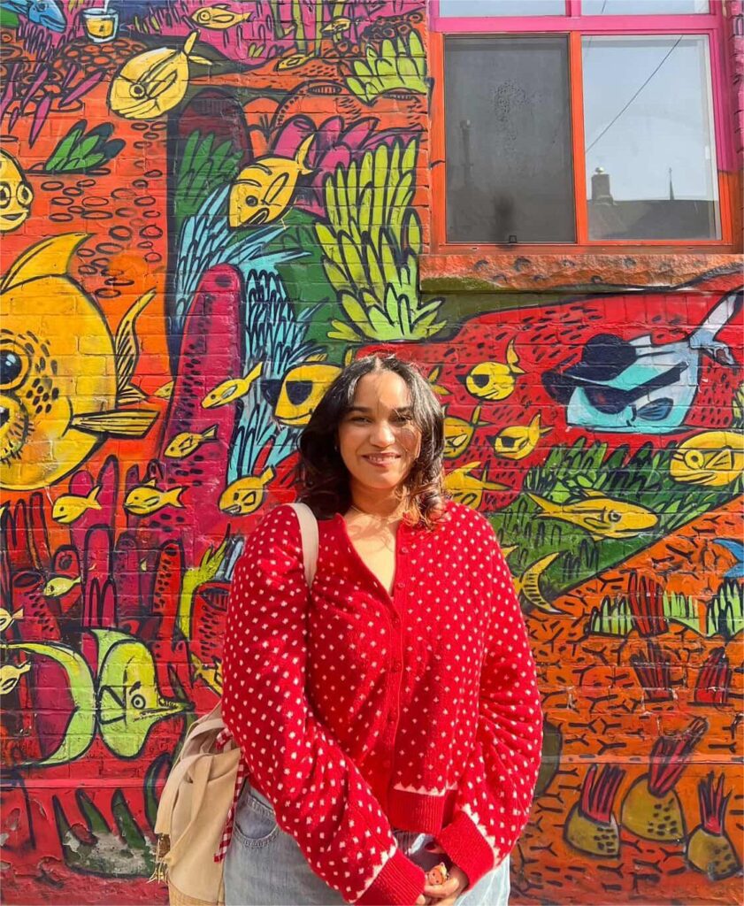 A woman is standing in front of a graffiti wall and smiling.