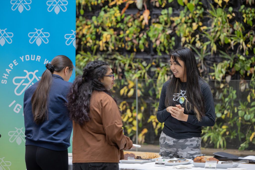 A woman stands behind the snack counter while two other women help themselves to some snacks.