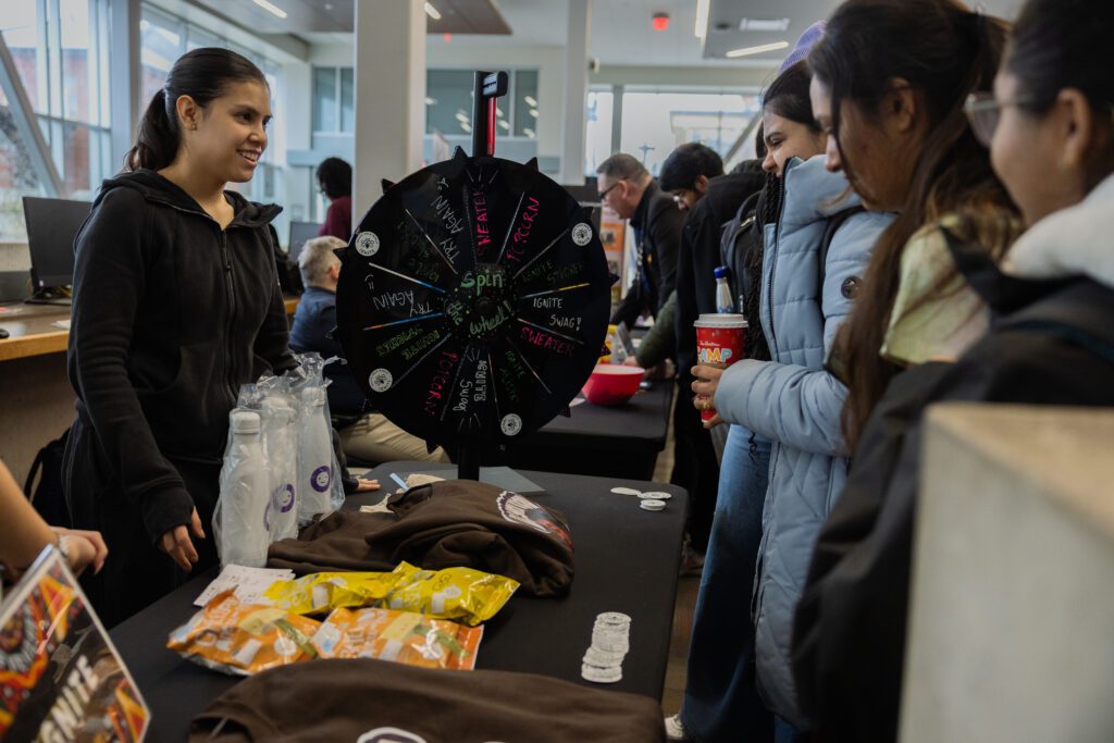 A woman is standing behind a counter, explaining a game to a group of students.