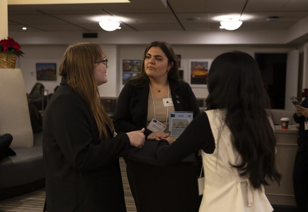 Three women in business attire are talking to each other during the Advocacy Summit.