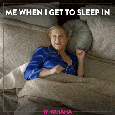 A woman in blue pajamas stretches happily in bed, with the text "ME WHEN I GET TO SLEEP IN".