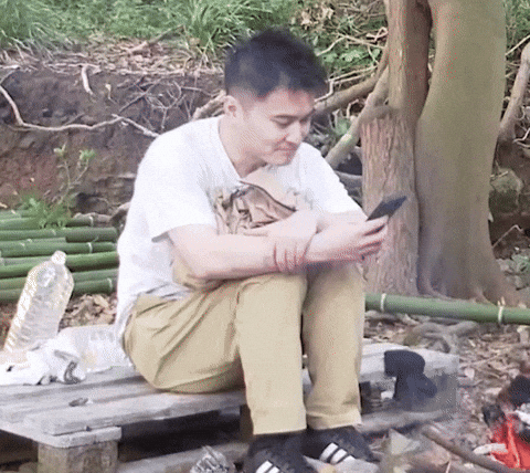 a man putting his phone down while sitting near a camp fire