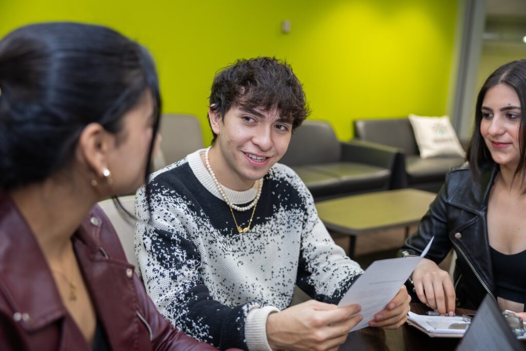 A man holding a piece of paper is looking at a woman with a smile on his face, while another woman is looking at him.