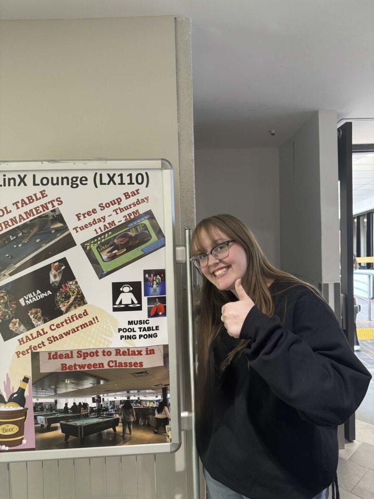 Student advocate Emily Edwards giving a thumbs up in from of a promotional IGNITE board