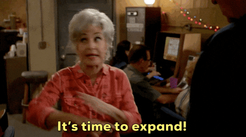 A woman with short gray hair excitedly gestures with her hands while saying, 'It's time to expand!