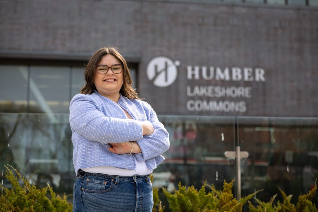 A woman is standing in front of Humber Polytechnic Lakeshore campus. 