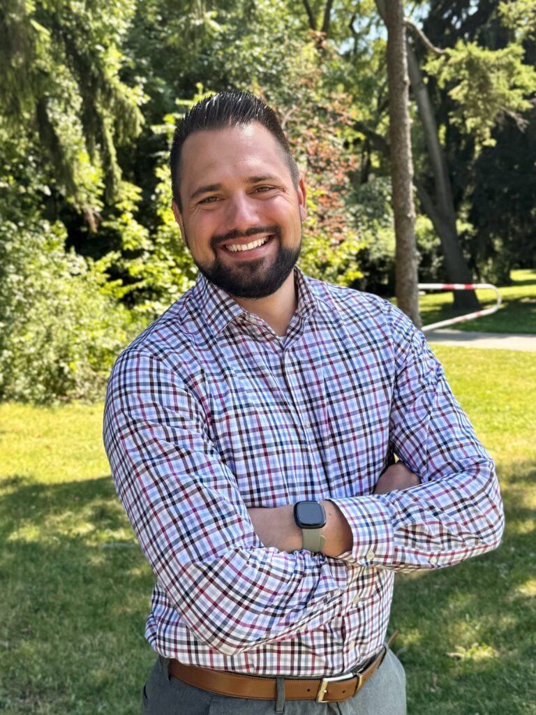 A man is standing in a garden and smiling.
