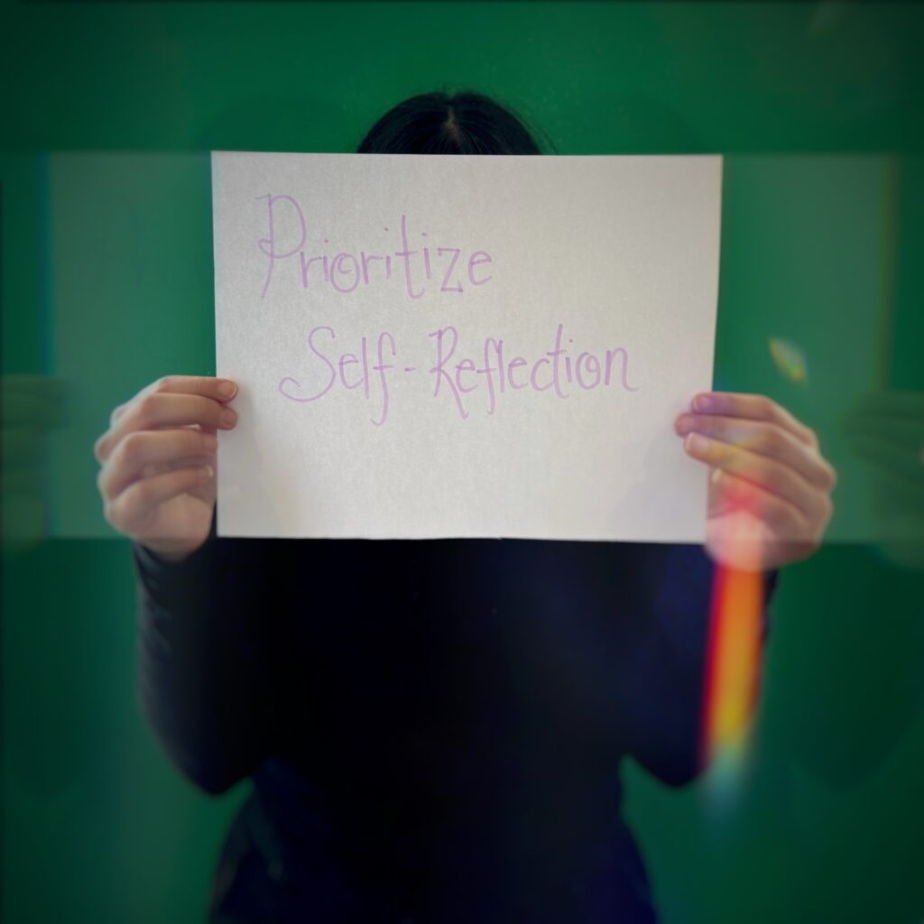A girl holding a paper saying "Prioritize Self-reflection".