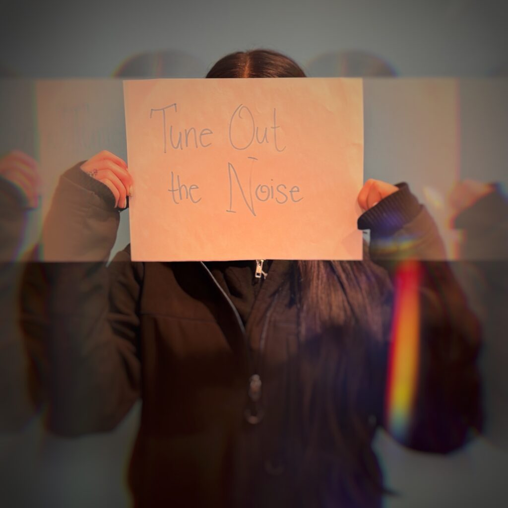 A girl holding a paper saying "Tune Out the Noise".