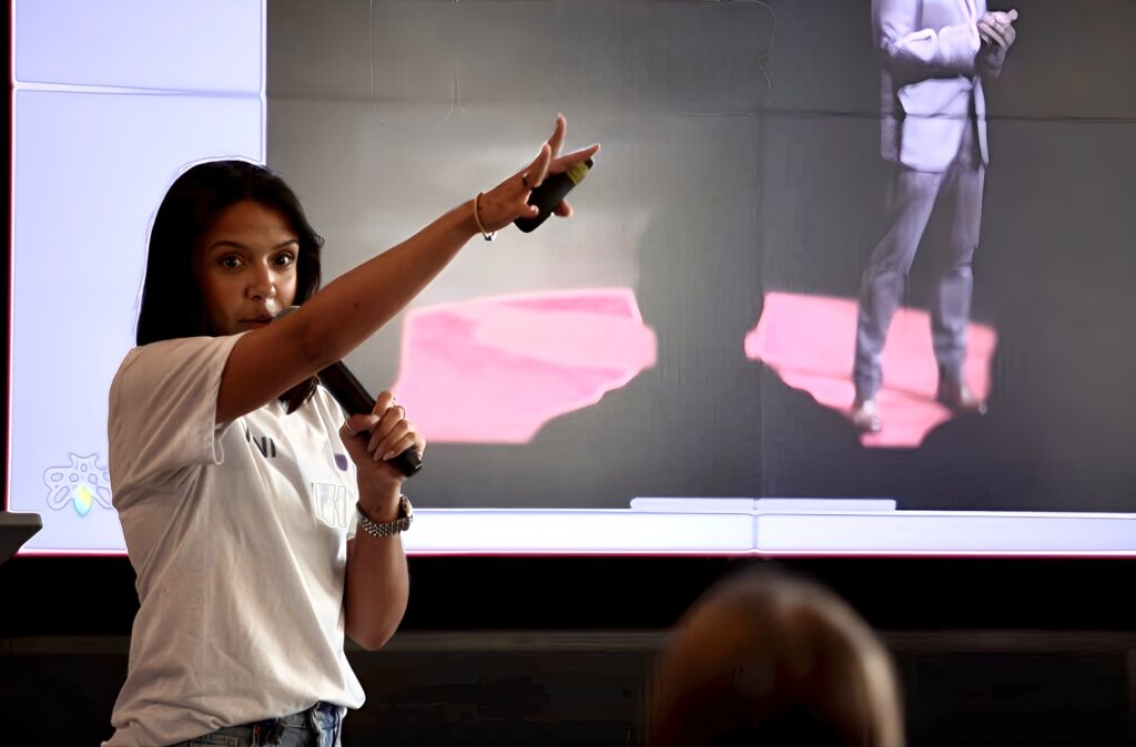 A picture of a girl raising her hands while talking to a group of people in public.