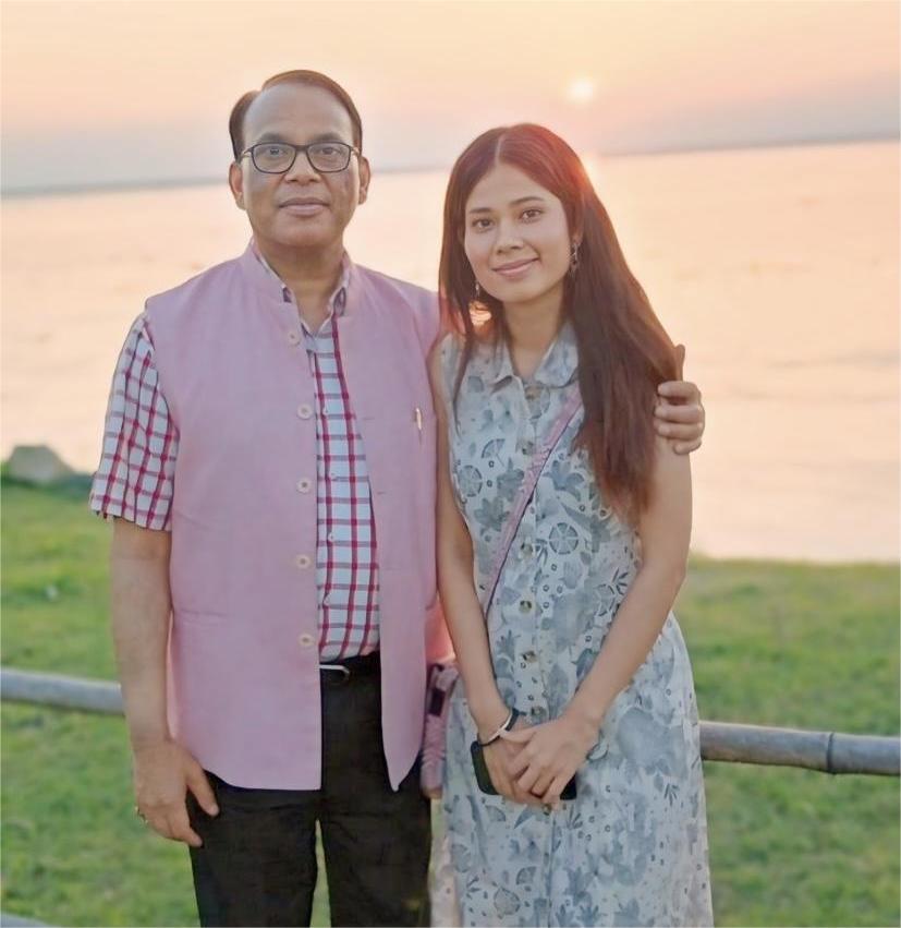 A father and daughter are standing together as the sun sets behind them.