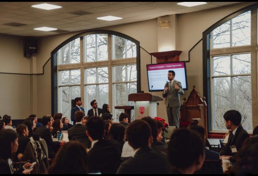 A man is giving a speech in front of a large class of students.