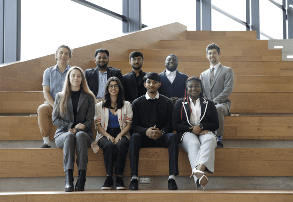 A group of students poses for a formal photo on modern wooden bleachers in a bright open space.