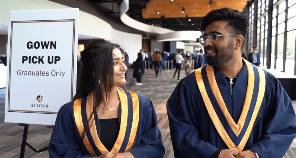 A man and woman in graduation gowns are talking to each other.