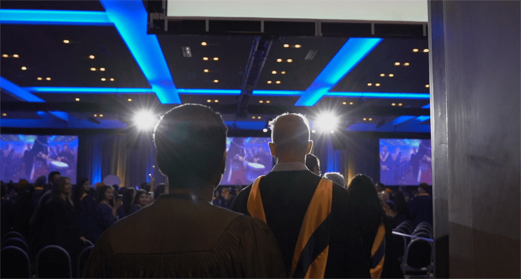 A group of people is walking into a hall lit by stage lights.