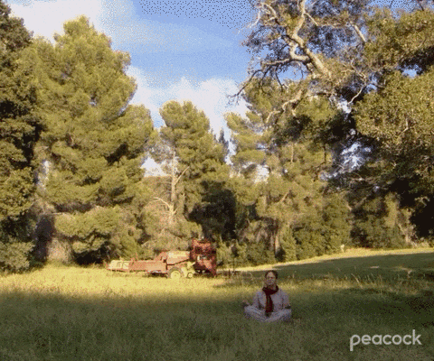 A quick zoom in on a man with glasses and red scarf, meditating in a park.