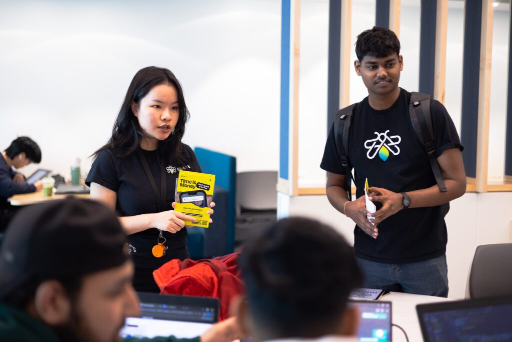Two people are talking to students while holding a poster from "Time Is Money" campaign.