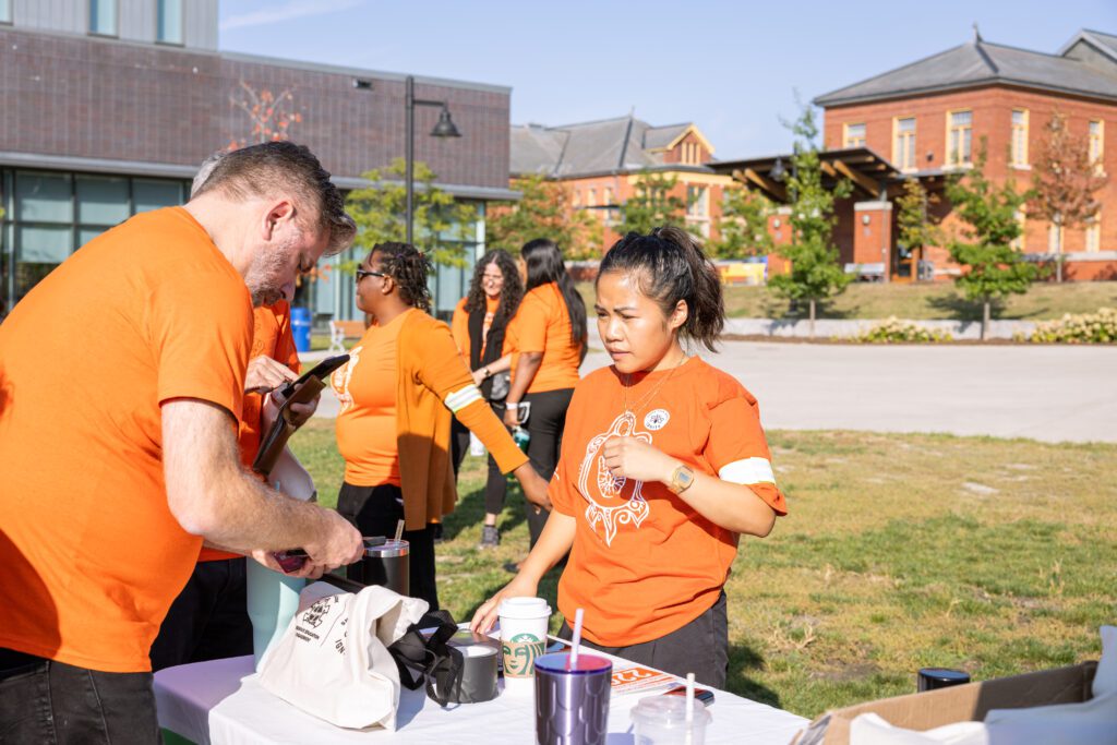 A group of people wearing orange t-shirts are gathered around a counter.
