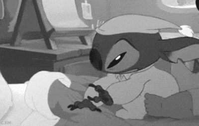 Stitch wearing pajamas and a night hat cuddling in bed with a stuffed animal.