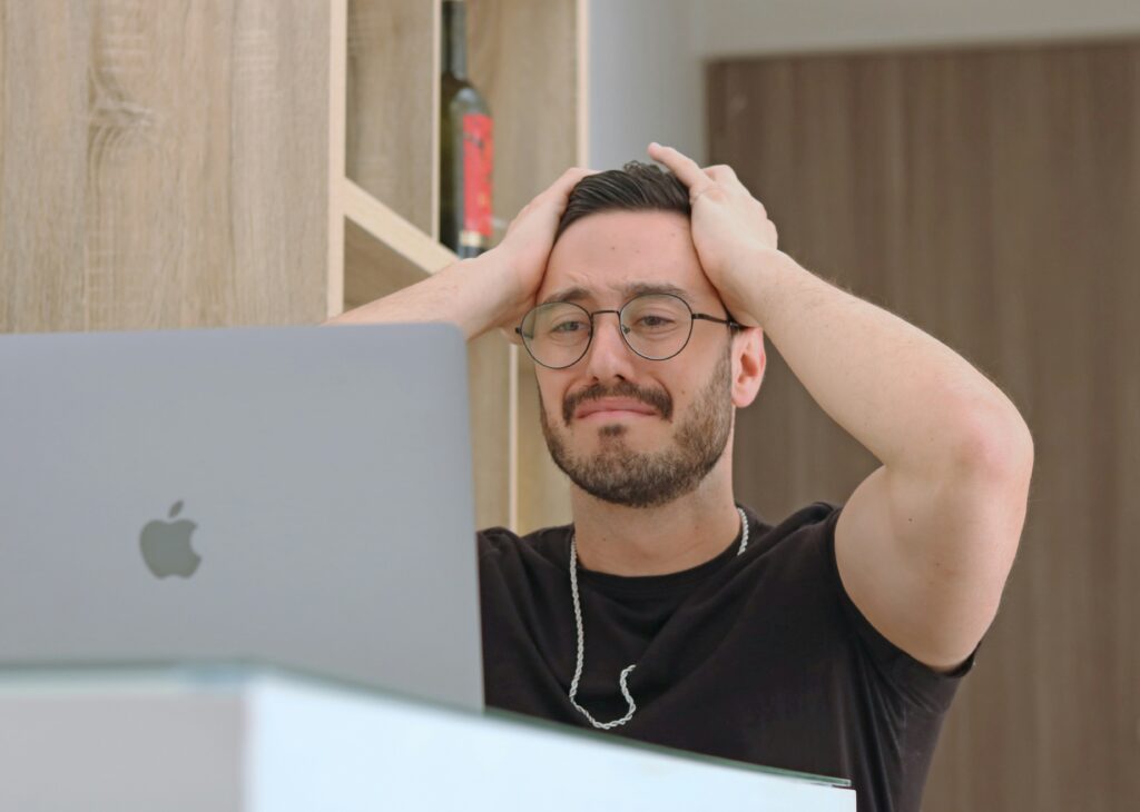 A person with a stressed look and hands on their head looking at a macbook screen.