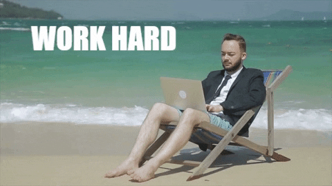 A man is working on his laptop at a beach and the words, "WORK HARD. PLAY HARD" are mentioned beside. 