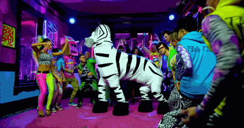 A group of people are dancing around someone dressed in a zebra costume.