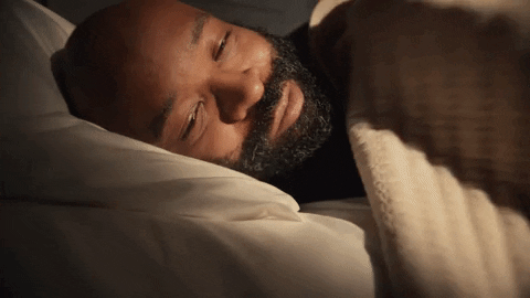 A man is pulling the blanket over and settling in to sleep.