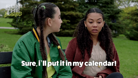 Two girls are sitting on a park bench and one is saying "Sure, I'll put it in my calendar! to the other one.