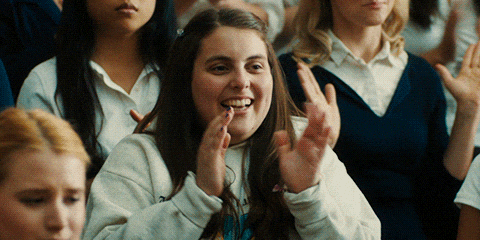 A woman is sitting among the crowd, giving a thumbs-up.