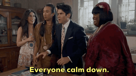 A group of people are standing tensely, while one man says, "Everyone calm down."
