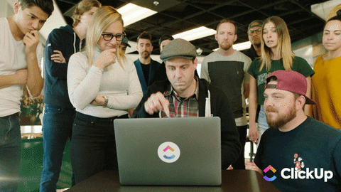 A man is clicking keys on a laptop and people are cheering behind him.