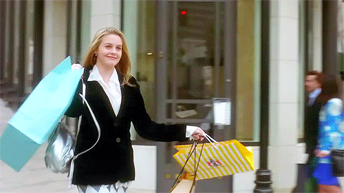 A girl is holding shopping bags as she crosses a street.