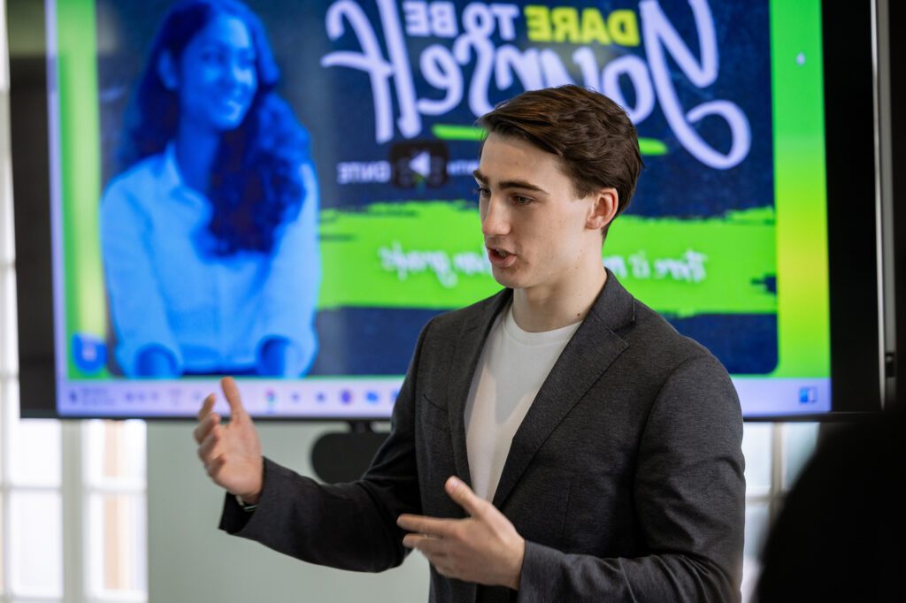 Former IGNITE Board of Director speaking at a Humber College campus event in front of a presentation screen.