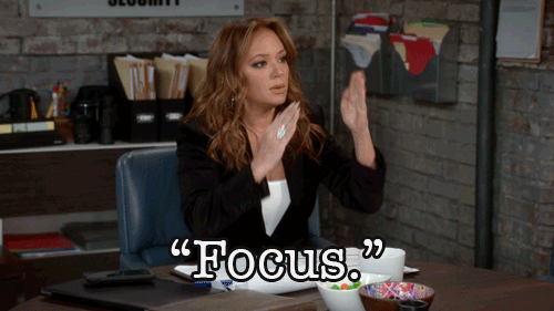 A girl in a black blazer gestures with both hands in an office setting, with the word "FOCUS".