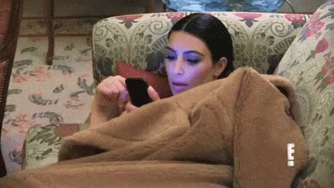Kim Kardashian laying on a couch while scrolling through her phone.
