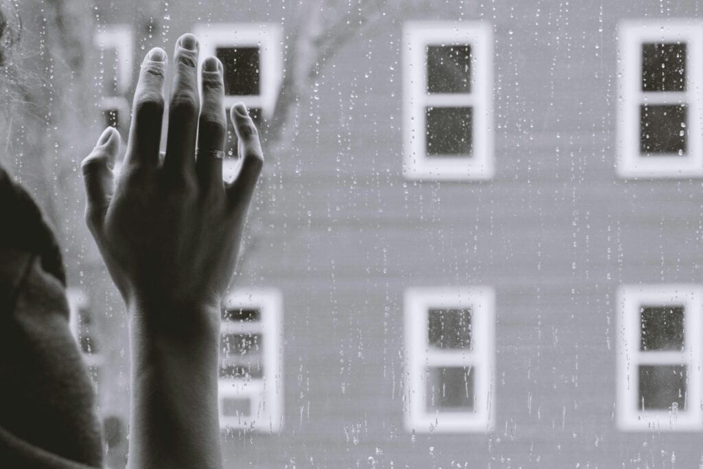 A hand on the inside of a raining glass window.