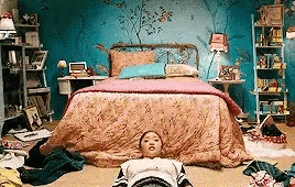 Lara Jean sits up from the floor, the background is set in her messy room.