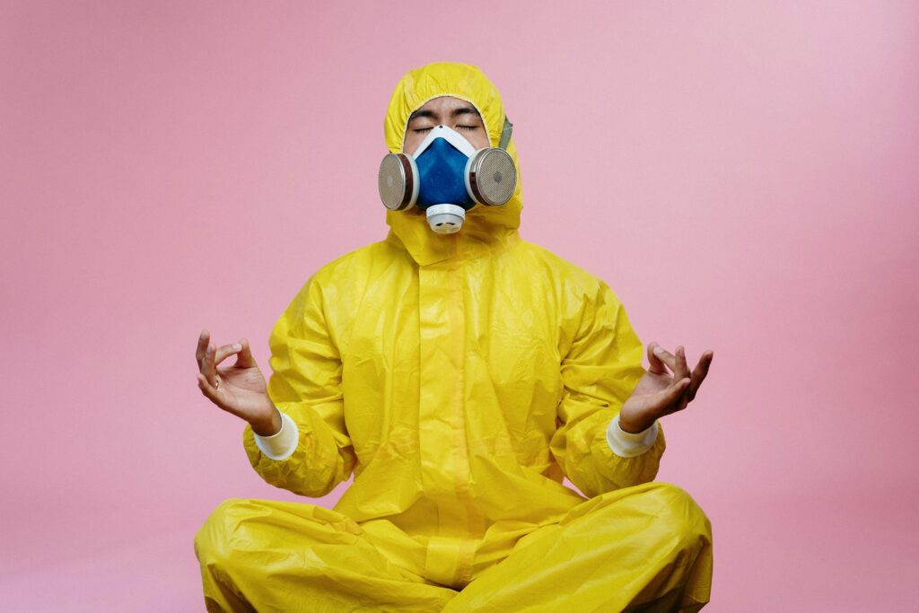 A person in a yellow hazmat suit in the traditional meditation pose. Cross legged and hands up with index fingers touching their thumb. 