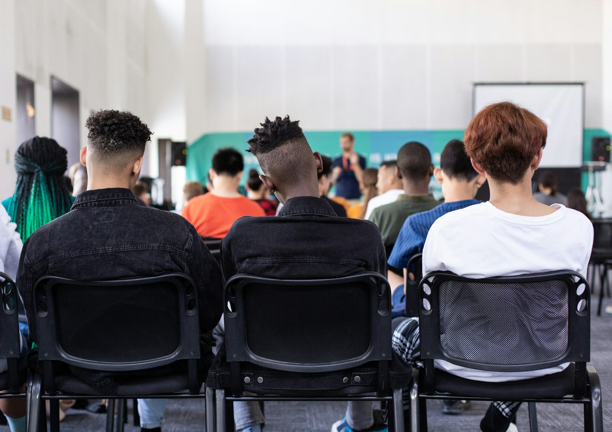 A picture of students taken from behind them, there are two sitting in a lecture hall with different style haircuts.