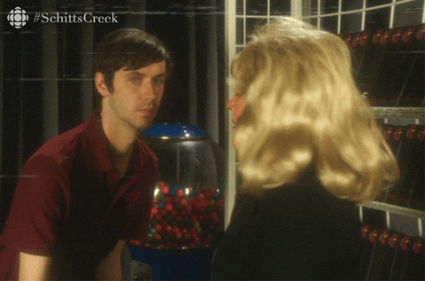 A woman with voluminous blonde hair and a young man in a red uniform looks surprised in the background, with the word "PAUSE".