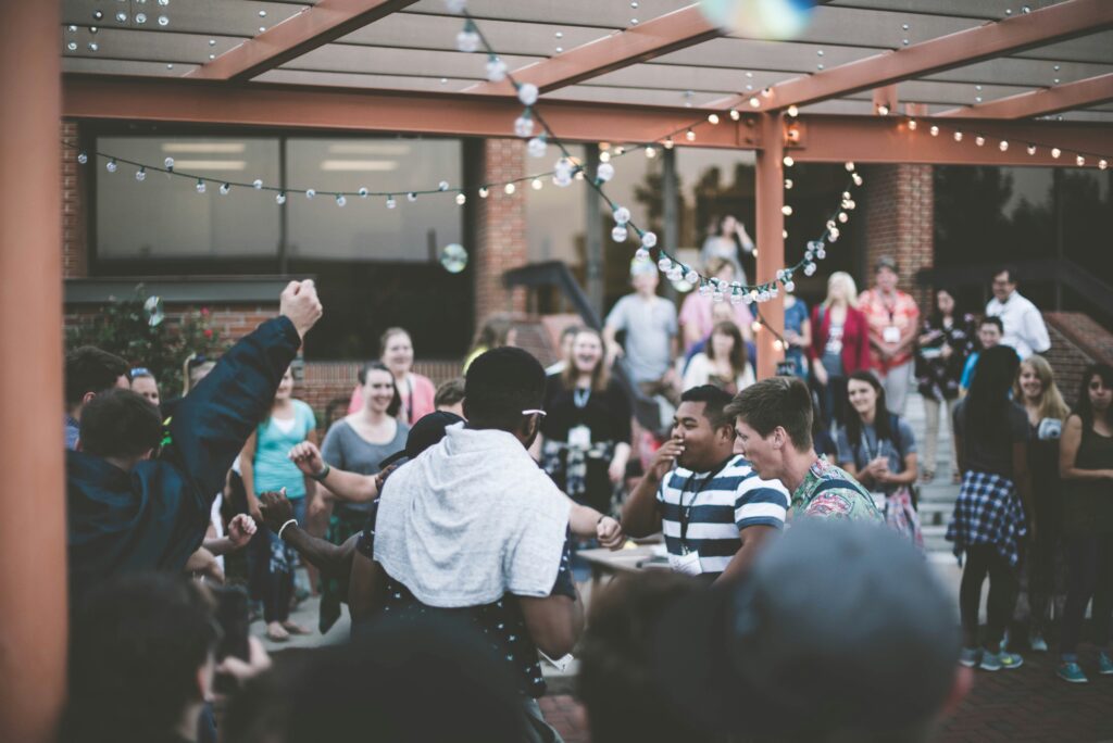 A large backyard gathering with people enjoying themselves. Fairy lights decorate the space. 