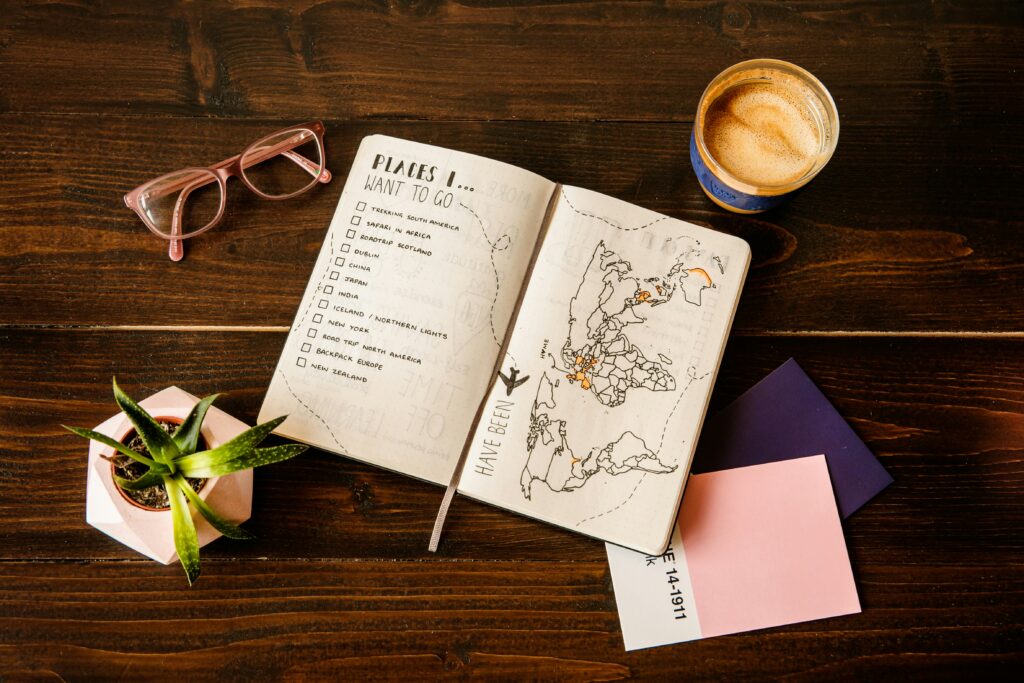 A book featuring a map and the words 'PLACES I WANT TO GO...' lies on a table beside a potted plant, a pair of glasses and a cup of coffee.