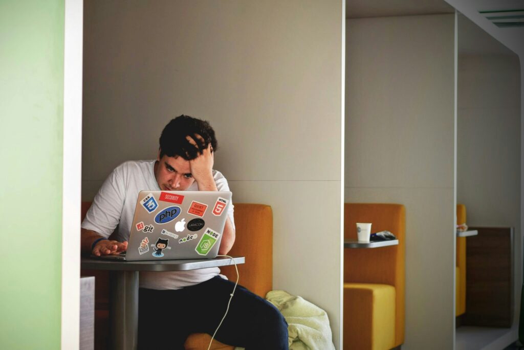 A man using his laptop has his hand on his head, looking worried.