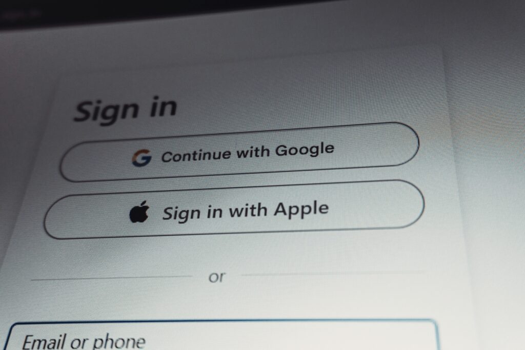 A computer screen displaying a sign-in page with options to Continue with Google and Sign in with Apple, each with their respective logos, above a field for entering email or phone information.