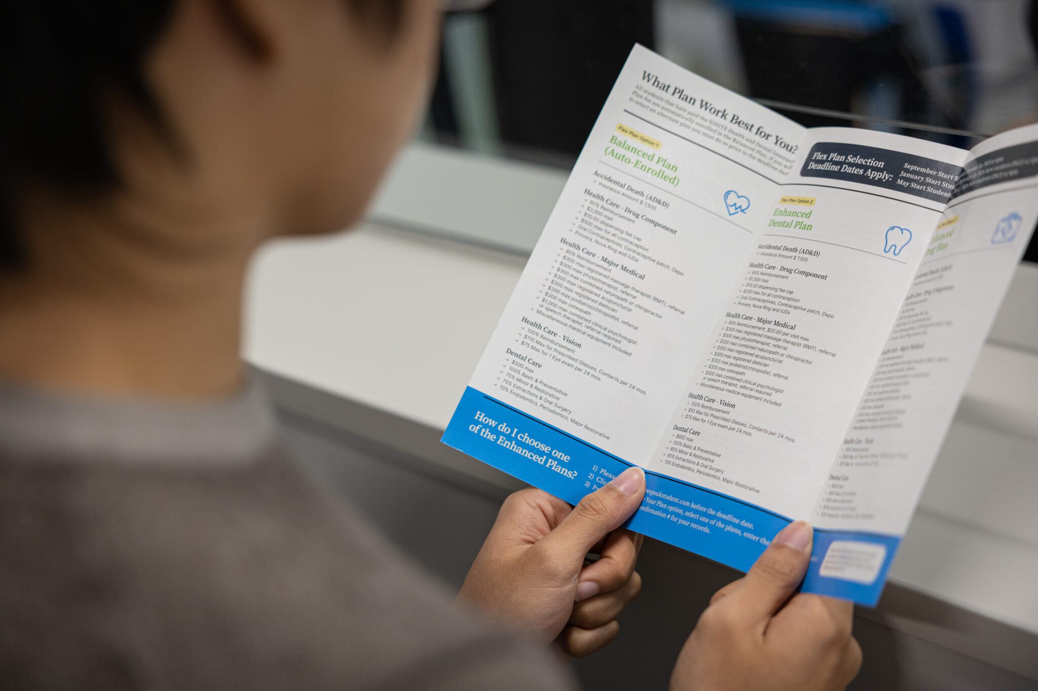 A person holding and reading a brochure about dental plan options, with sections listing benefits, coverage details, and comparison between different dental plans. The text on the brochure is partially visible.