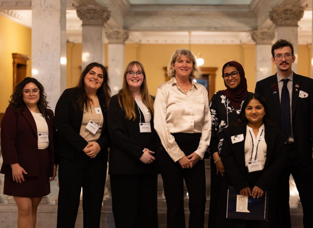 Group of seven professionals in business attire posing for a formal group photo in a marble hallway with columns.