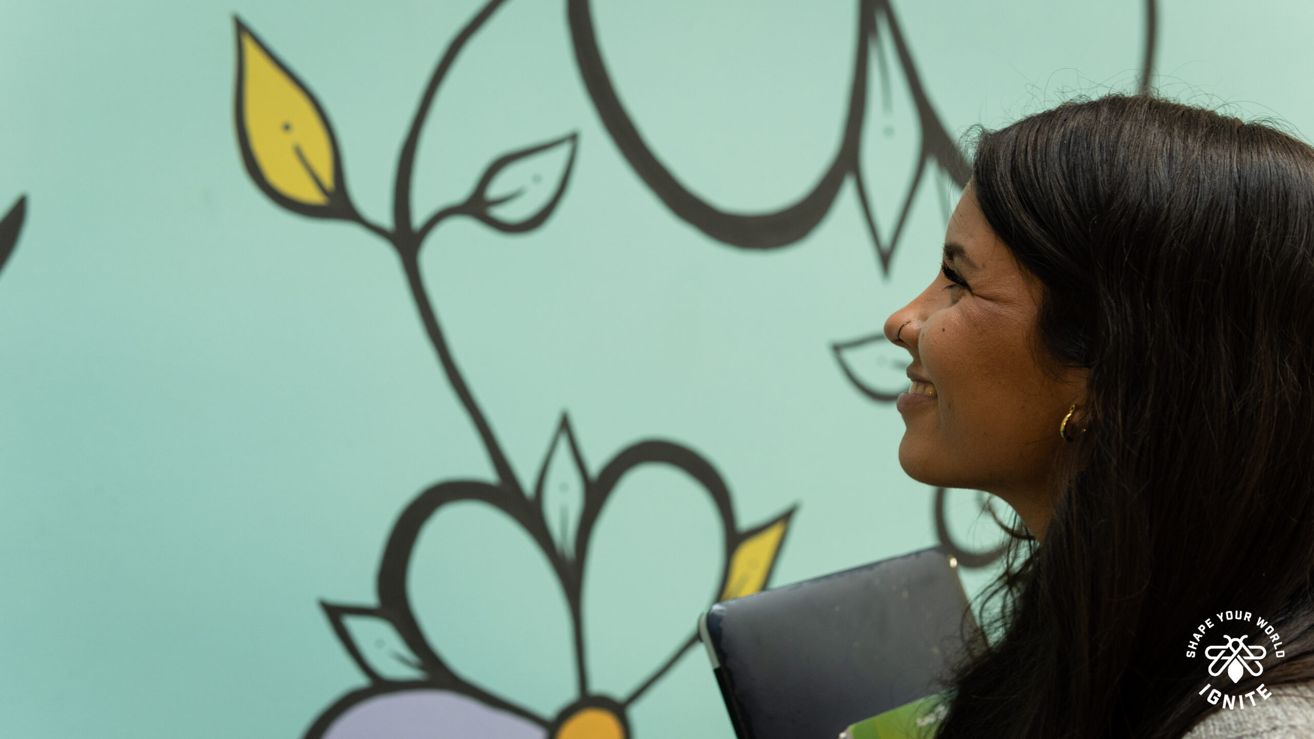 A post-secondary student smiling at a mural with flowers, stems and leaves.