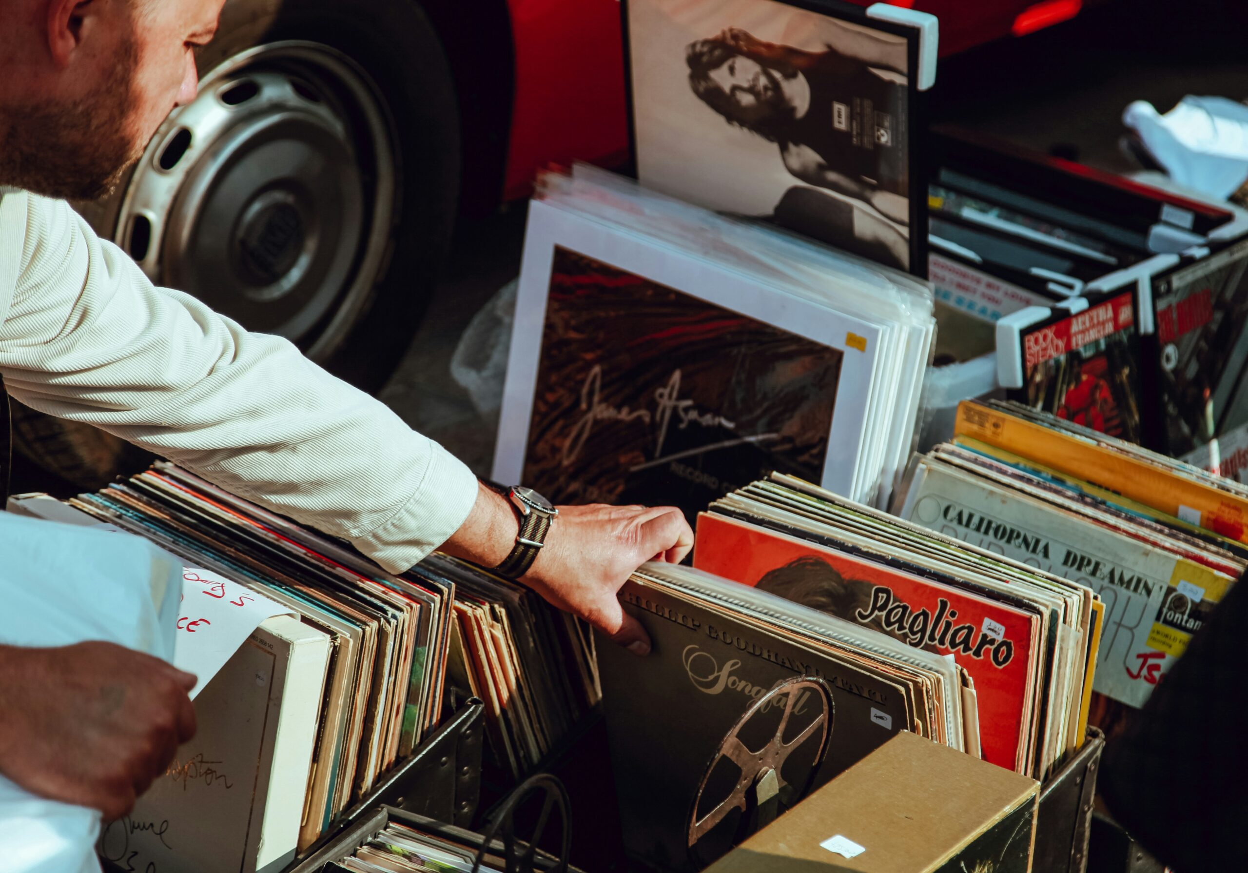 A person's hand sifting through vinyl records in boxes piled next to each other.