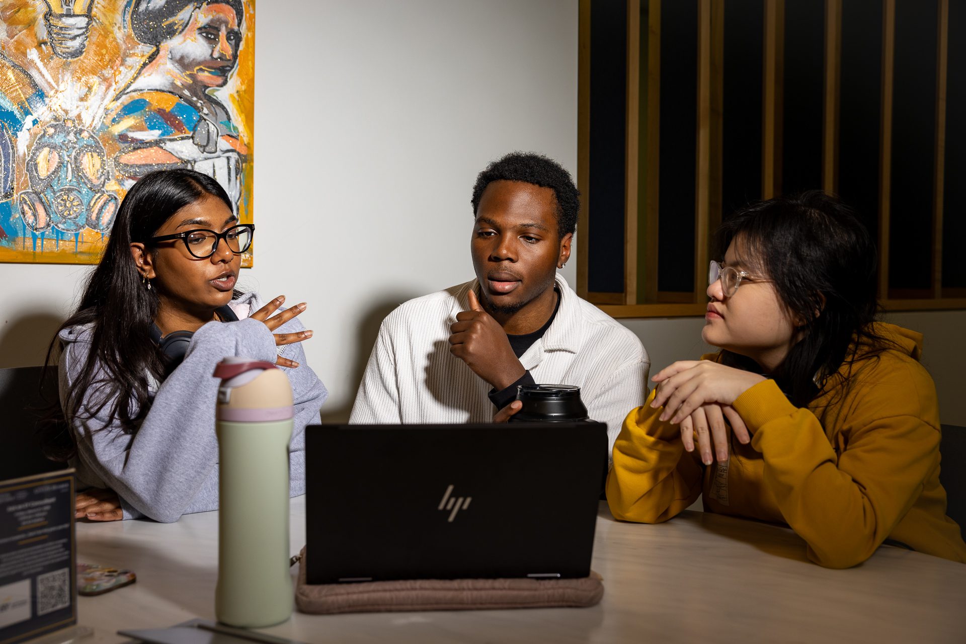 Three students sitting around a laptop discussing work together at a table.